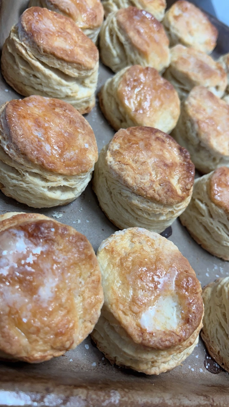 Sheet pan of tall flaky buttermilk biscuits with buttered golden tops